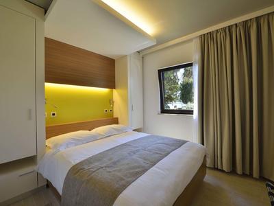 Pequeña habitación de hotel con cama doble, cabecero de madera y ventana con cortinas