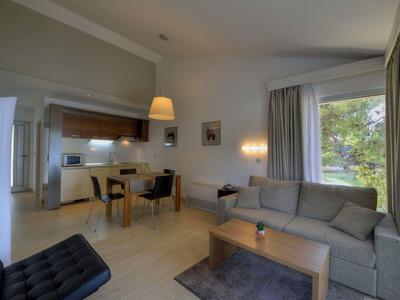 Sala moderna con sofá, mesa de centro y comedor junto a ventana grande con vista a la naturaleza.