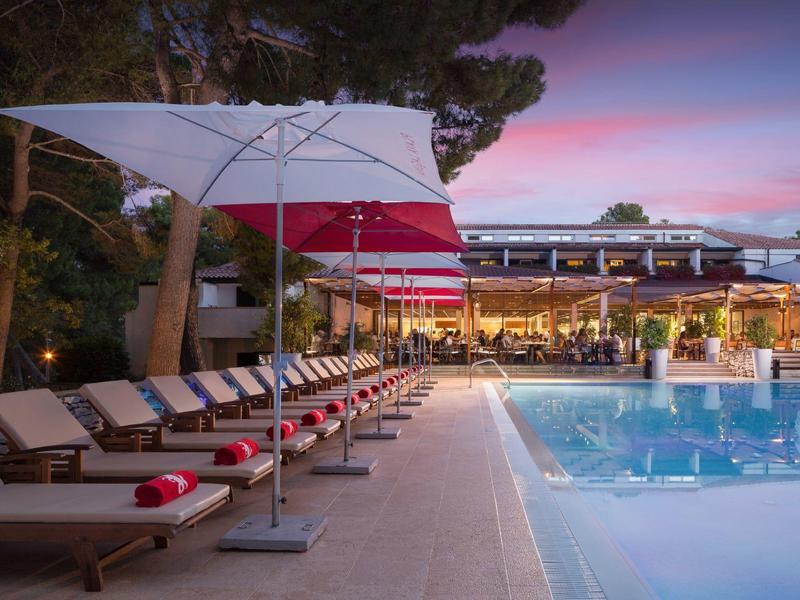 Verlicht hotelzwembad met ligstoelen en parasols bij zonsondergang.