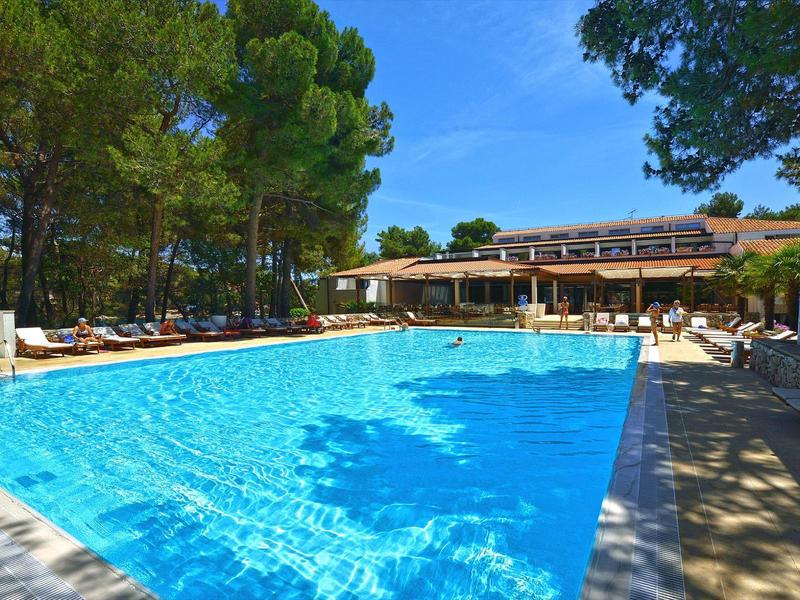 Groot hotelzwembad met ligstoelen en bomen onder blauwe lucht.