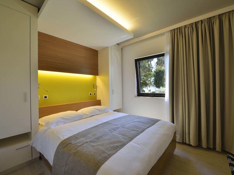 Helder hotelkamer met tweepersoonsbed, houten paneel en indirecte verlichting.