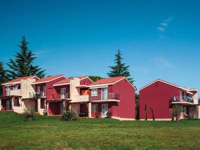 Case vacanza rosse con balconi e prato verde sotto un cielo azzurro.