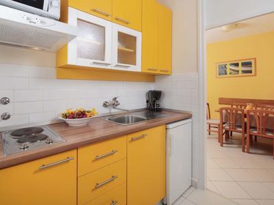 Piccola cucina gialla con fornello, lavello e vista sulla zona pranzo adiacente.