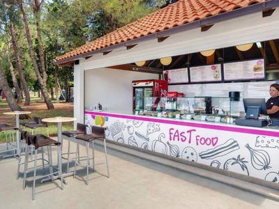 Zona de asientos al aire libre frente a un puesto de comida rápida con techo rojo en un parque.
