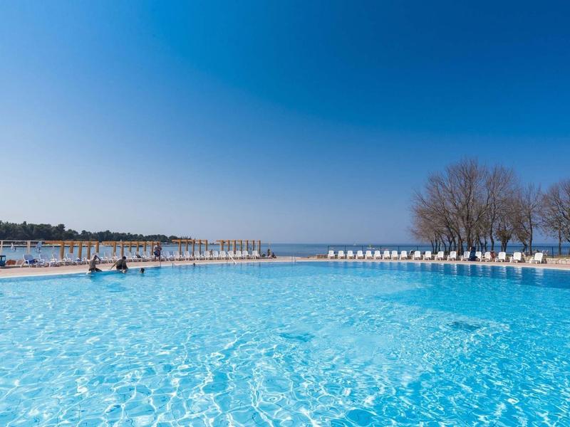 Grande piscina all'aperto con acqua cristallina e lettini lungo il bordo sotto un cielo sereno.