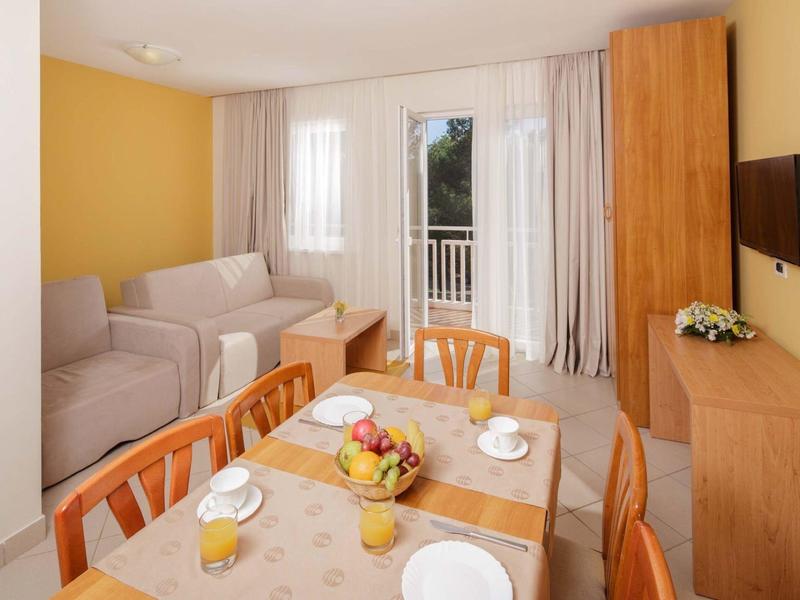 Soggiorno e sala da pranzo luminosi con mobili in legno, divano, tavolo con frutta e balcone sullo sfondo.