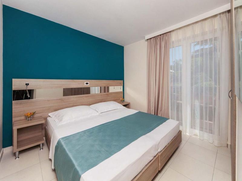 Camera d'albergo moderna con letto matrimoniale, parete blu accentata e tende chiare.