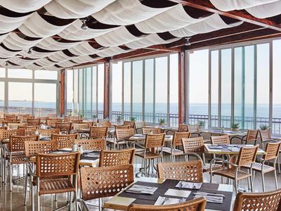 Gran comedor con muchas mesas y sillas, grandes ventanas y vista al mar.