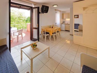 Cocina-salón luminosa con mesa de comedor, zona de estar, TV y acceso a balcón con sillas.
