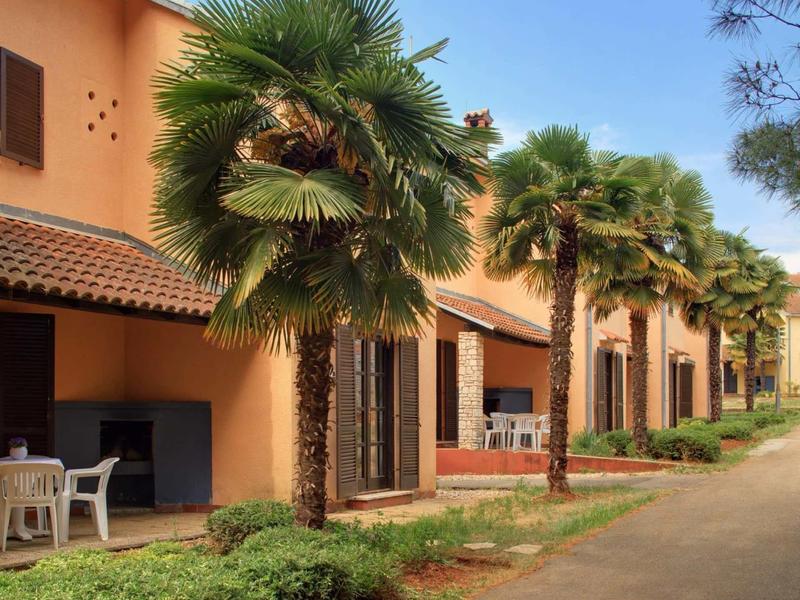 Edificio dell'hotel con bungalow in fila, circondato da palme e un vialetto sotto.