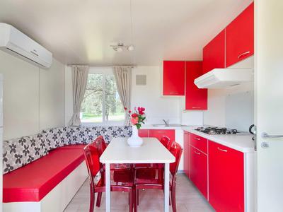 Moderne keuken met rode kasten, witte tafel en bankje bij het raam.