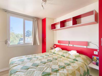 Lichte slaapkamer met groot raam, rood hoofdeinde en modern wandrek.