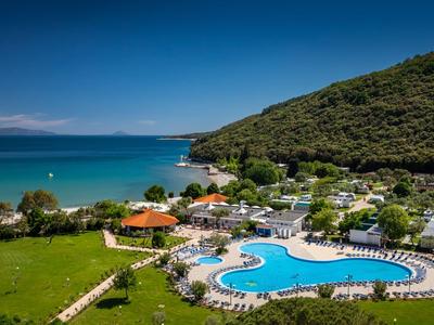Hotelanlage mit großem Pool, Sonnenliegen, grüner Wiese und Meerblick unter klarem Himmel.