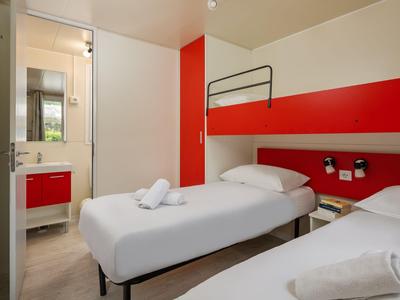 Modernes Hotelzimmer mit zwei Einzelbetten, rotem Akzent und angrenzendem Badezimmer.