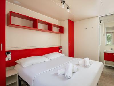 Modernes Hotelzimmer mit Doppelbett, roten Akzenten und Bad mit Spiegel.