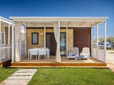 Modernes Ferienhaus mit Veranda, weißen Möbeln und Liegestühlen auf Holzterrasse.