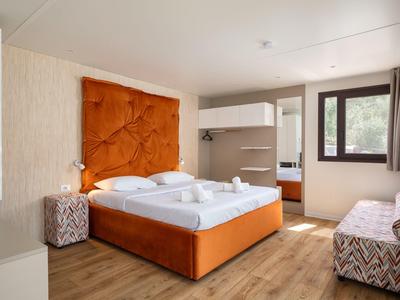 Hotelzimmer mit Doppelbett, orangefarbenem Kopfteil, Holzboden und Sitzbereich mit Sofa.