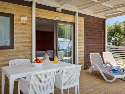 Terrasse mit weißem Tisch, Stühlen und Liegestühlen vor einem Holzhaus im Urlaub.