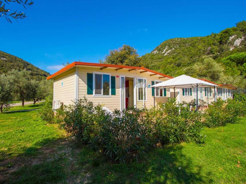 Dwa domki letniskowe z tarasami na zielonym terenie pod jasnym niebieskim niebem.