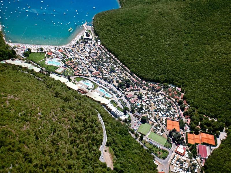 Małe nadmorskie miasteczko z gęsto zabudowanymi domami między lasem a niebieskim morzem.