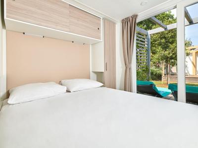 Przytulna sypialnia z łóżkiem podwójnym i widokiem na basen i ogród przez duże szklane okna.