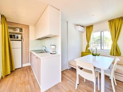 Jasna, nowoczesna przestrzeń mieszkalna z małą kuchnią i stołem jadalnym obok okien z żółtymi zasłonami.