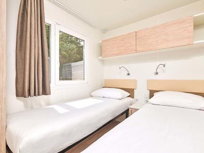 Prosty pokój z dwoma pojedynczymi łóżkami, oknem i drewnianymi szafkami na ścianie.