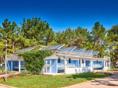 Nowoczesny niebiesko-biały dom wakacyjny z panelami słonecznymi, otoczony drzewami i zielonym trawnikiem.