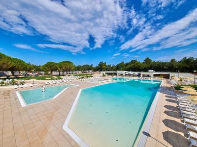 Duży basen na świeżym powietrzu z leżakami i jasnym niebieskim niebem w ośrodku wypoczynkowym.