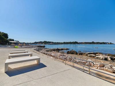 Nowoczesna nadbrzeżna przestrzeń z ławkami i widokiem na spokojne morze pod przejrzystym niebem.