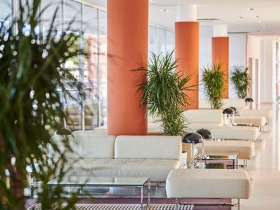 Světlá hotelová lobby s bílými pohovkami, zelenými rostlinami a oranžovými sloupy.