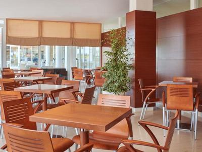 Moderní restaurace s dřevěnými židlemi a stoly, velkými okny a rostlinami.