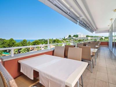 Velká terasa s stoly a židlemi, výhled na zelenou krajinu a moře.