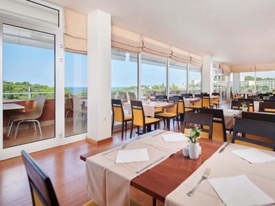 Světá restaurace s stolem, židlemi a velkými okny s výhledem na zeleň.