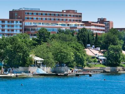 Velká hotelová budova u břehu jezera s rostlinami a přístavištěm pro lodě.