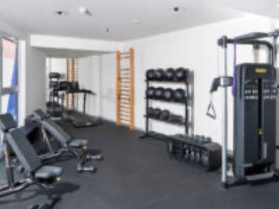 Moderní posilovna s různými tréninkovými stroji a činkami před bílými zdmi.