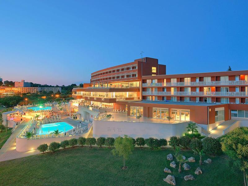 Moderní hotelový komplex s venkovním bazénem a osvětlenými cestičkami za soumraku.