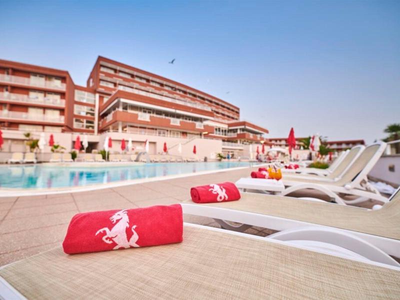 Hotel s velkým venkovním bazénem a lehátky s červenými ručníky za slunečného dne.