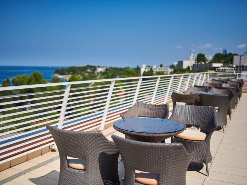 Prázdné stoly a židle na hotelové terase s výhledem na moře za slunečného dne.