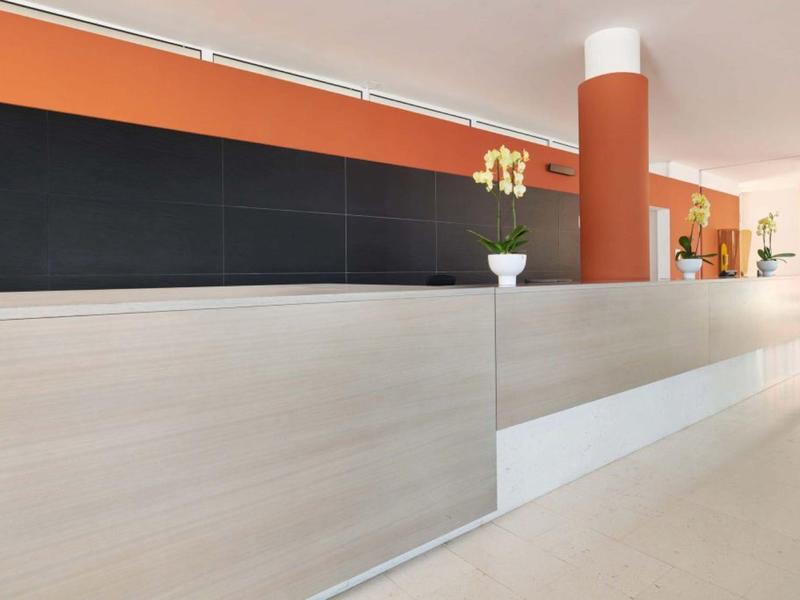 Moderní hotelová recepce s dlouhým béžovým pultem a oranžovou stěnou v pozadí.