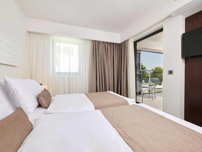 Jasny pokój hotelowy z dwoma łóżkami, neutralnymi kolorami i widokiem na taras.