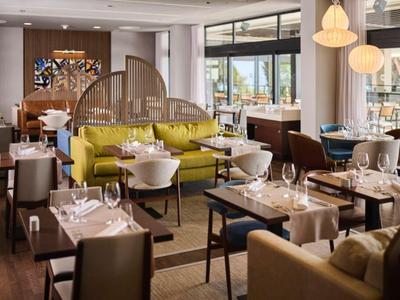 Salle à manger d'hôtel moderne avec tables, chaises et séparateur de pièce décoratif.