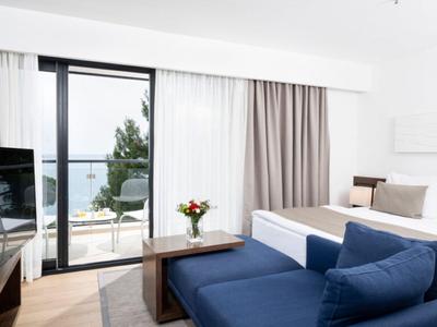 Chambre d'hôtel lumineuse avec un grand lit, des canapés bleus et vue sur la terrasse et la mer.