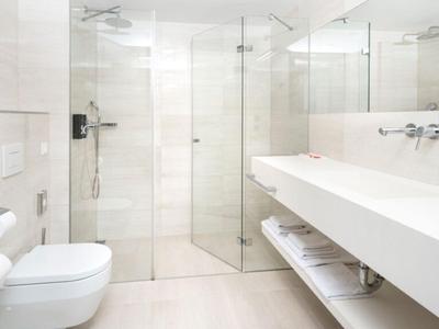 Salle de bains lumineuse et moderne avec douche en verre, toilette murale et long lavabo avec miroir.