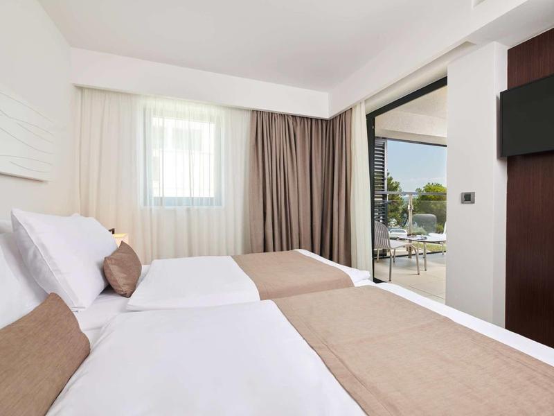 Nowoczesny pokój hotelowy z dwoma pojedynczymi łóżkami, dużym oknem i balkonem z widokiem na wodę.