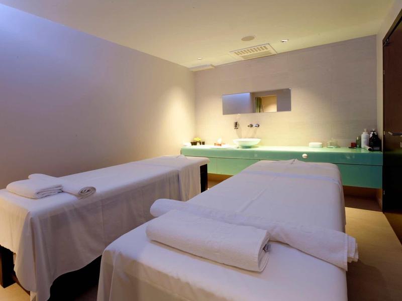 Dwa stoły do masażu z białymi ręcznikami w spokojnym, delikatnie oświetlonym pokoju spa.