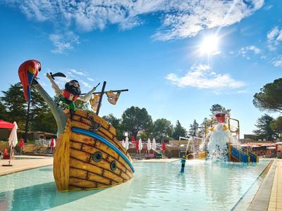 Bunte Wasserattraktion mit Piratenschiff und Fontänen in einem Hotelpool unter blauem Himmel.