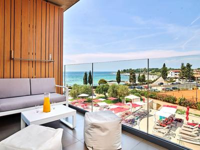 Balkon mit moderner Möbelgruppe, Blick auf Strand mit Sonnenschirmen und blauem Meer.