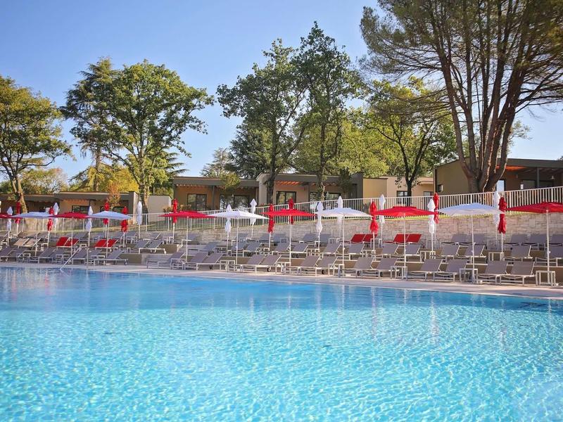Piscine bleue claire avec des parasols blancs et des arbres en arrière-plan.