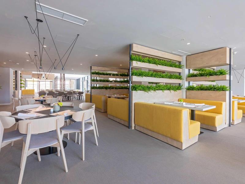 Restaurant moderne avec banquettes jaunes, chaises blanches et murs végétaux décoratifs.